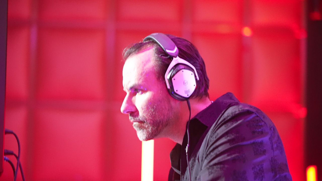 A DJ in headphones in profile against the red padded wall