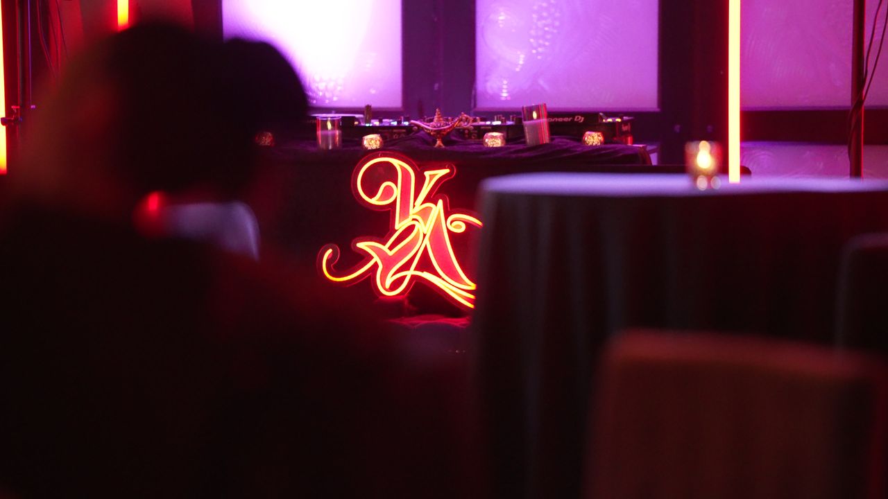 The neon KYA logo glowing behind cocktail tables