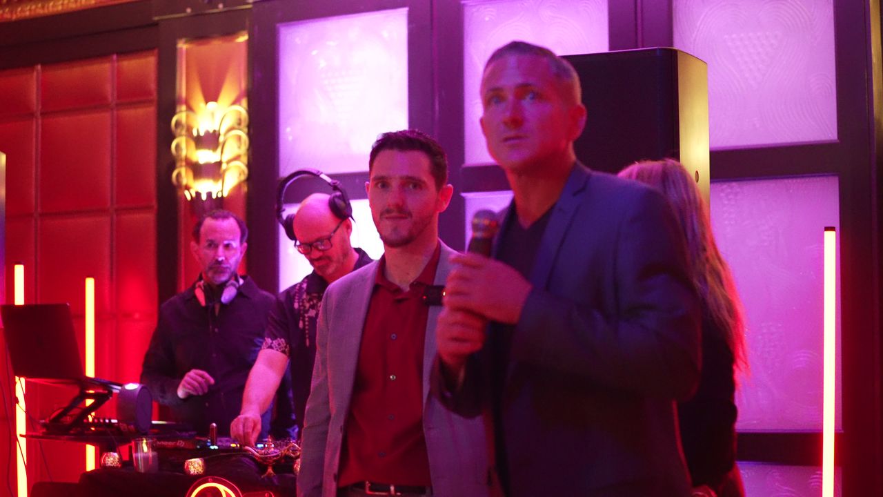 Justin Meyers and a guest speaker on the mic in front of the DJ booth
